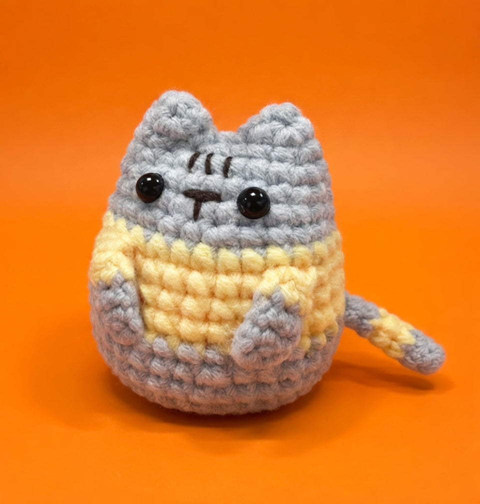 Crocheted cat toy with gray and yellow colors on an orange background